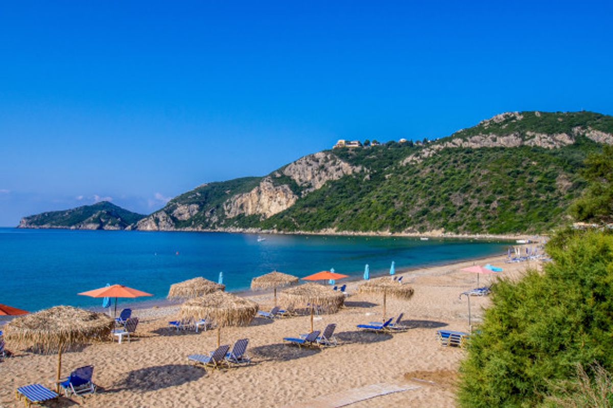 The striking backdrop of Agios Georgios Beach on the island of Corfu, lined with sunloungers and straw umbrellas