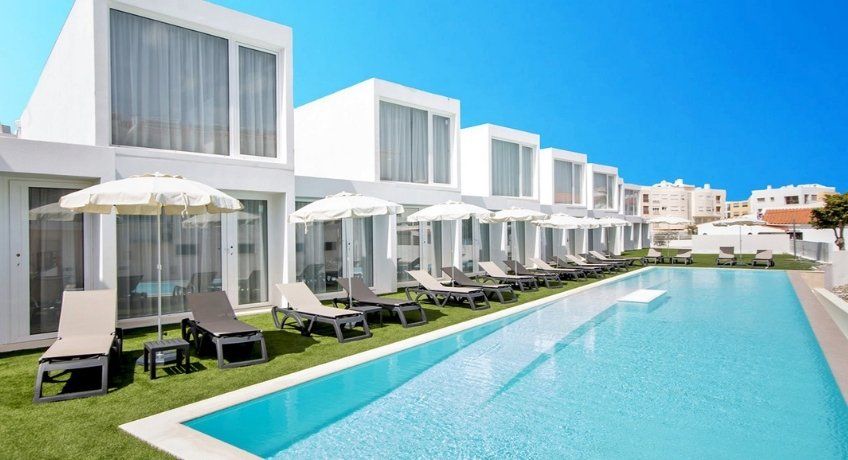 Large blue outdoor pool lined with sun loungers with a bright blue sky and buildings in the background