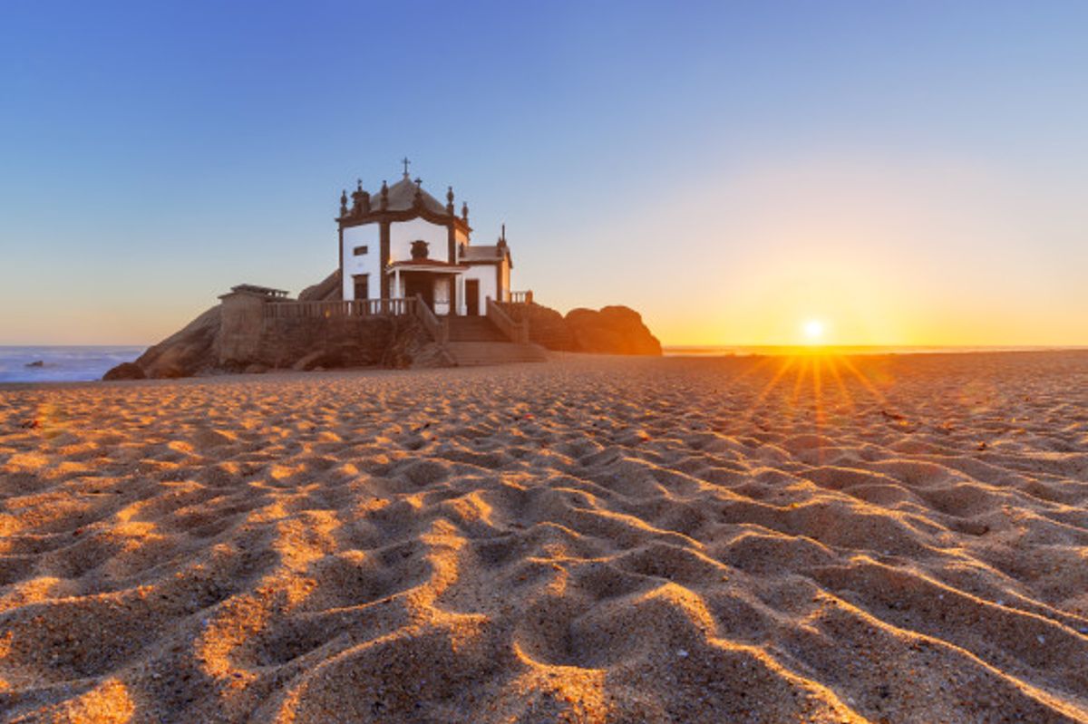 The striking Praia de Miramar in Portugal at sunset with rippled sands and a traditional chapel in the distance