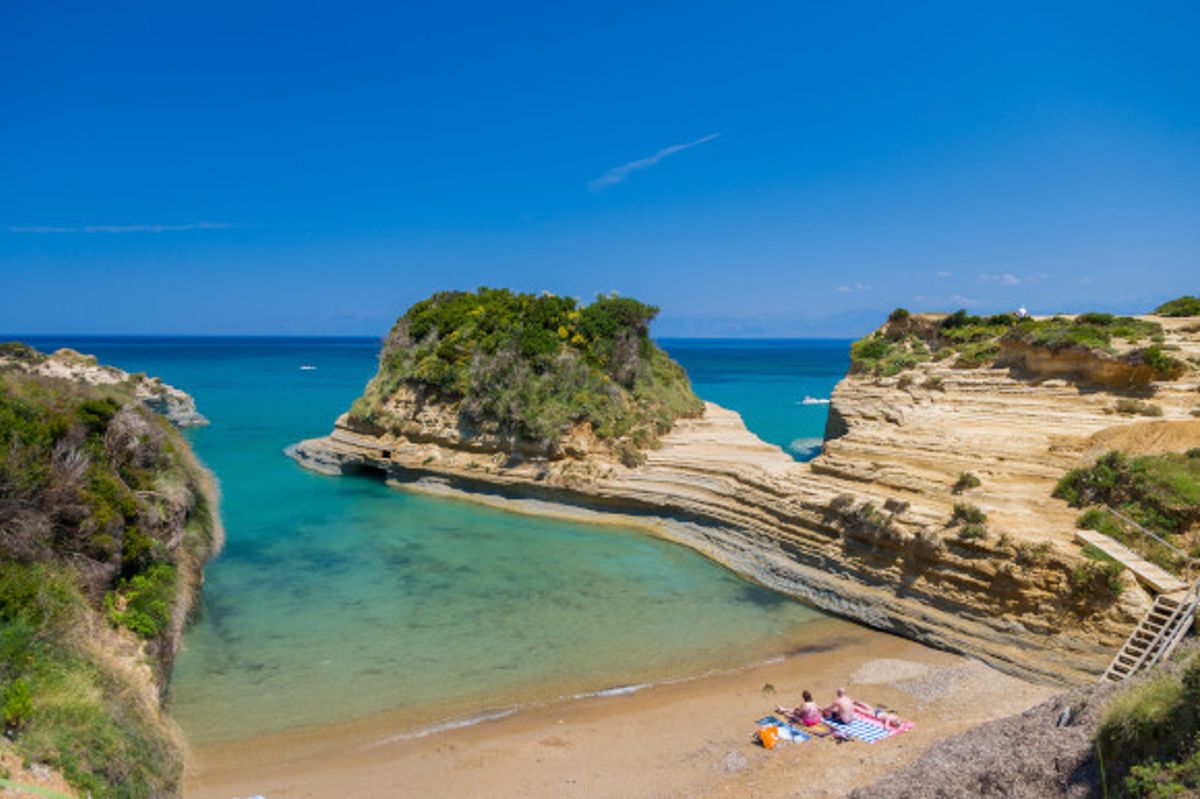 A beautiful beach in Sidari, Corfu with two sunbathers sitting on the sand