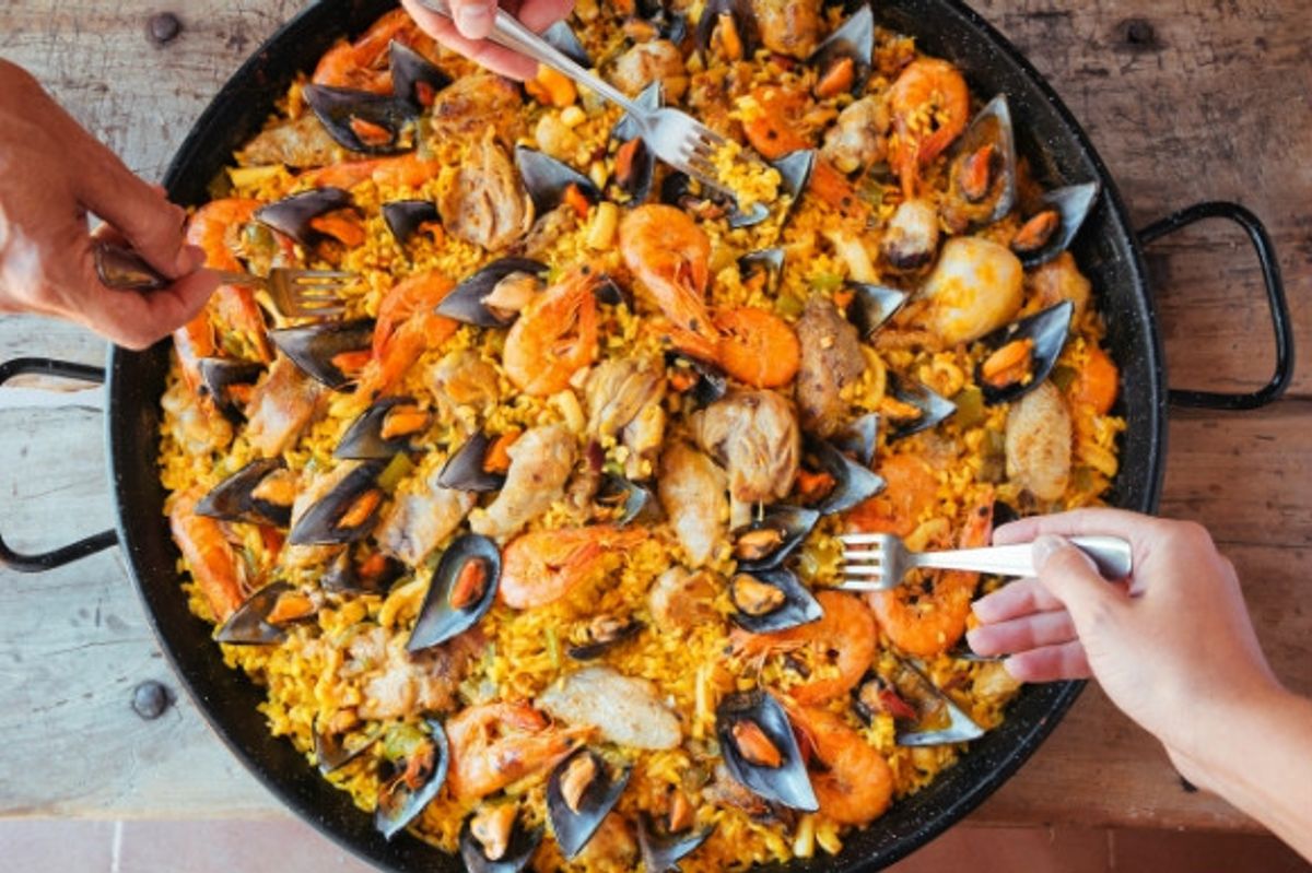 Forks tucking into a tasty bowl of seafood Paella in Spain.