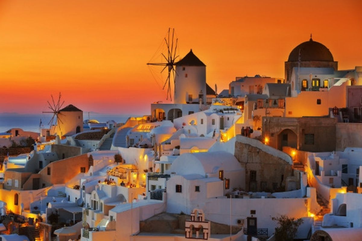 The golden backdrop of the sun setting over the whitewashed resort of Oia in Santorini, Greece.