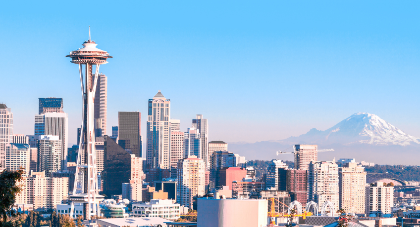 Seattle skyline with the Space Needle in the foreground, high-rise buildings across the city, and Mount Rainier visible in the distance under a clear blue sky.