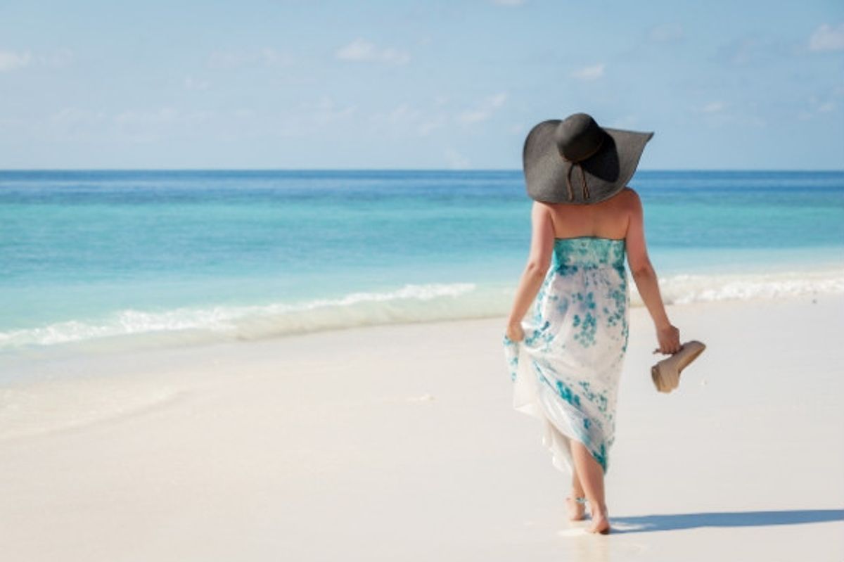 Woman walking barefoot along the white stretch of sand.