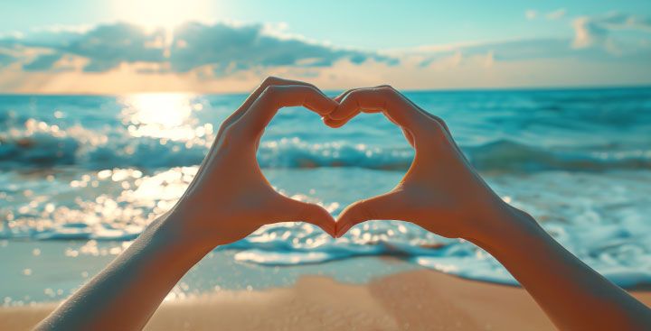 Hands making heart shape with sea in background