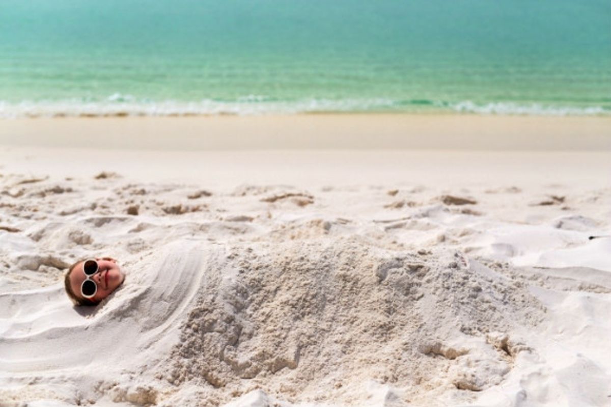 Little girl with sunglasses buried under the sand on the beach.