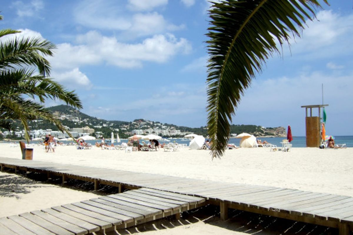 A stunning, soft white sand beach in Talamanca on the island of Ibiza, backed by a wooden promenade and palm trees