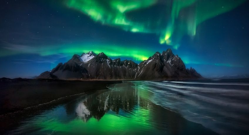 The northern lights in the evening over a hill with icy river