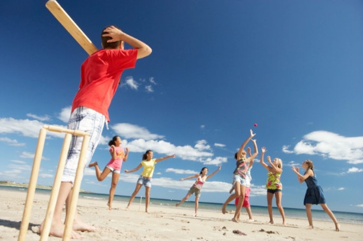 Kids playing cricket on the beach on a sunny day.