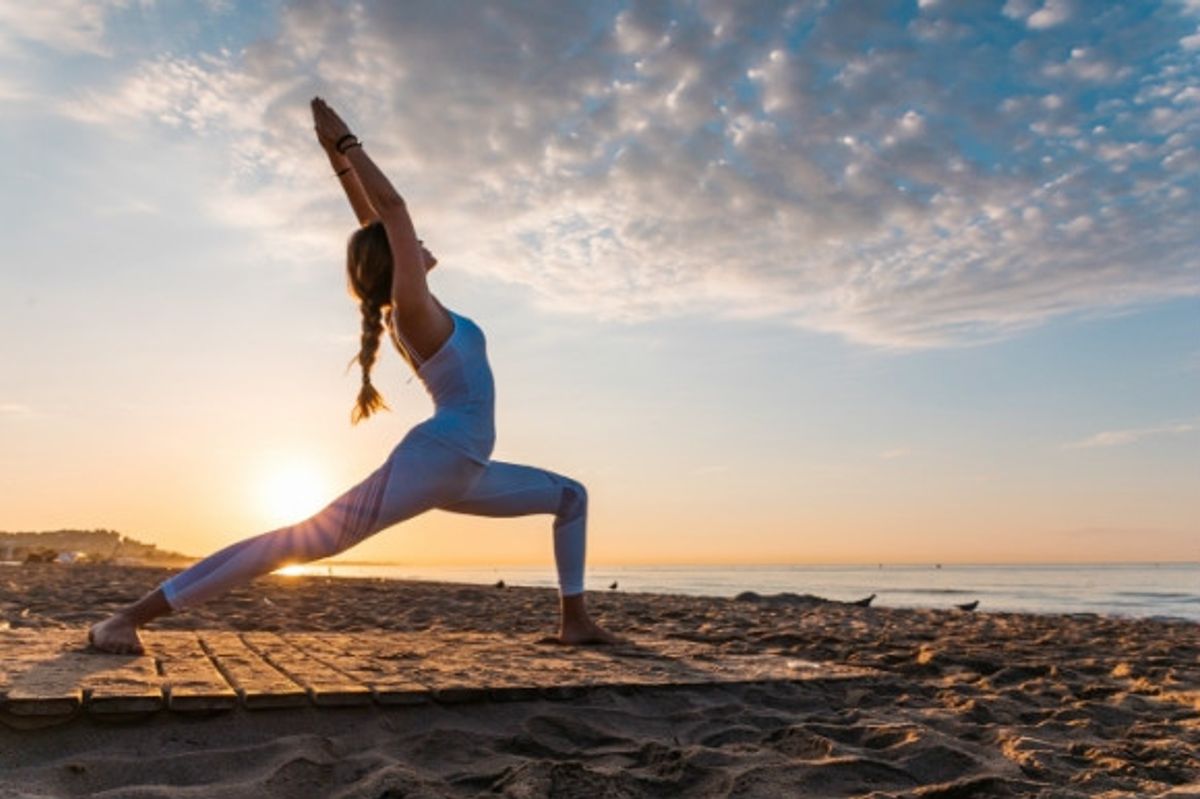 A woman doing yoga on the beach in the morning with the sunrise in the background.