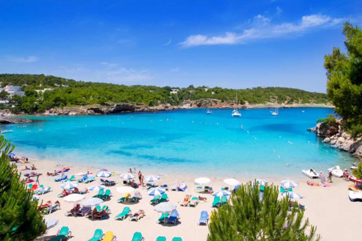 A stunning cove in the resort of Portinatx on the island of Ibiza with white sands and azure waters surrounded by green cliffs