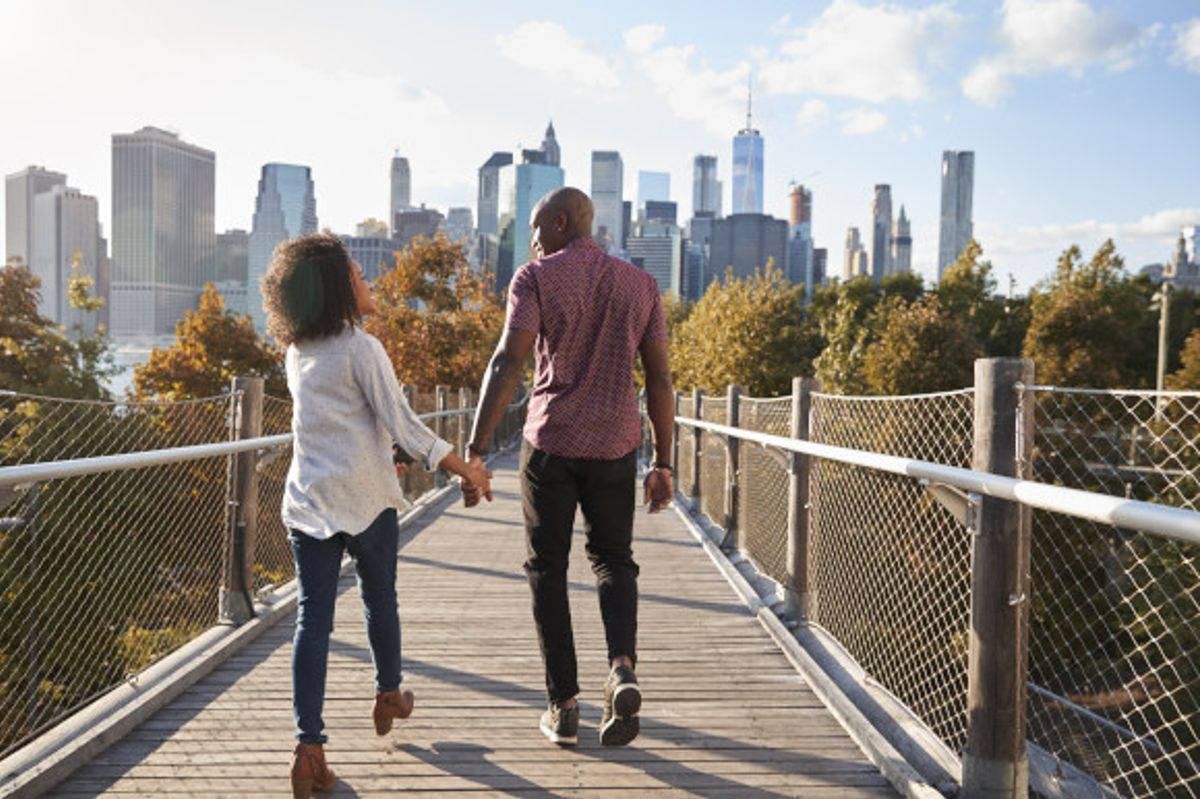 Couple holding hands as they stroll across a bridge with New York City's iconic skyline surrounding them