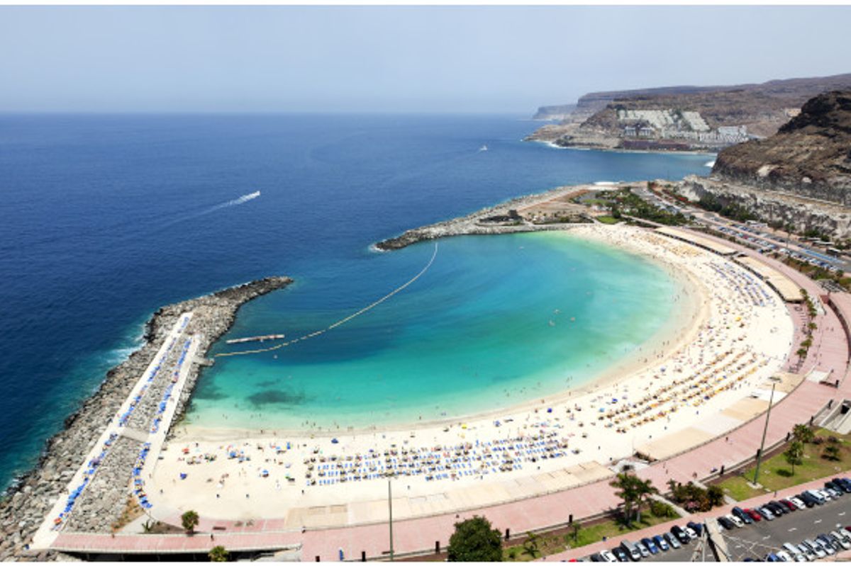 A high up view of the curved, white sand and emerald water at Playa de Amadores Beach in Gran Canaria