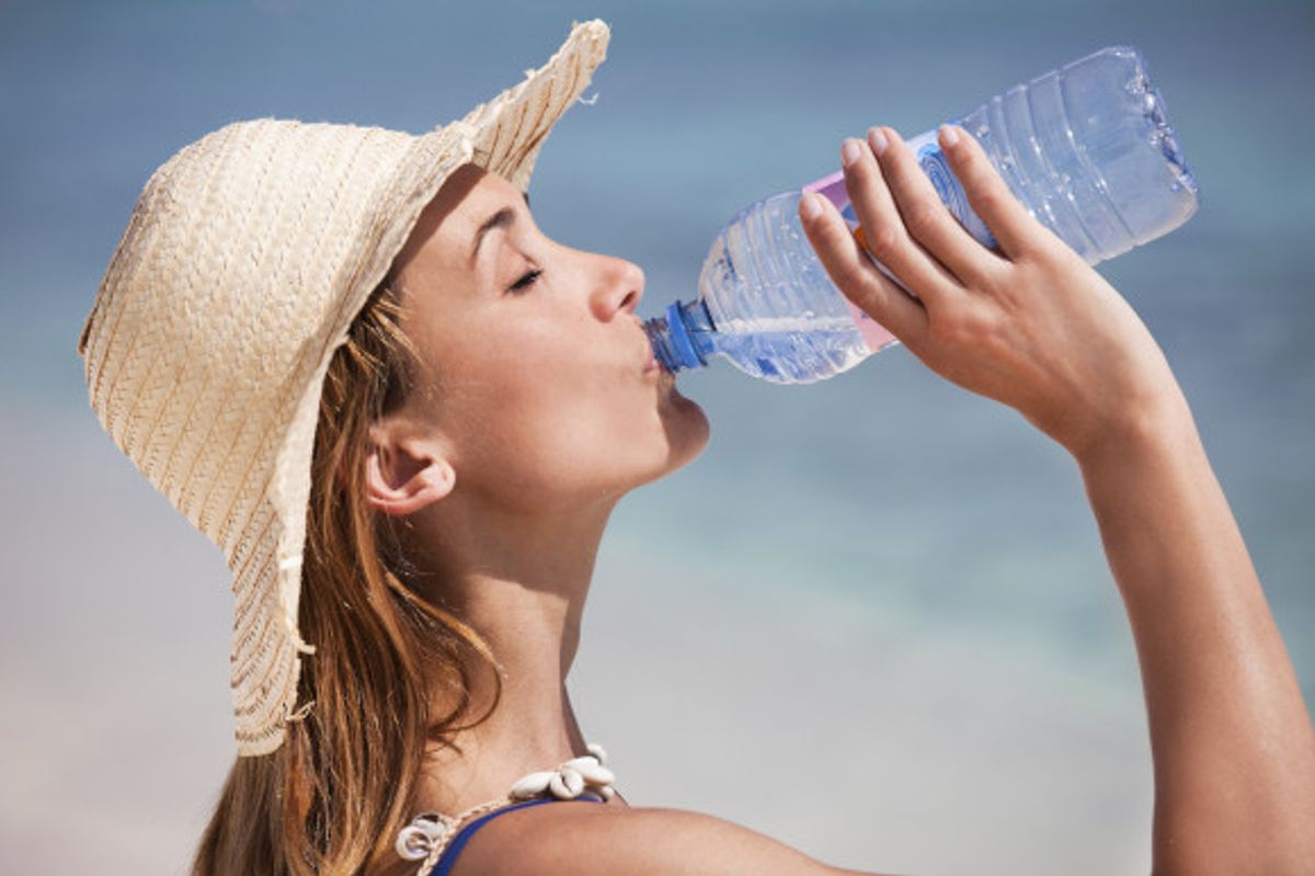 Woman in a hat enjoying a refreshing drink of water on the beach