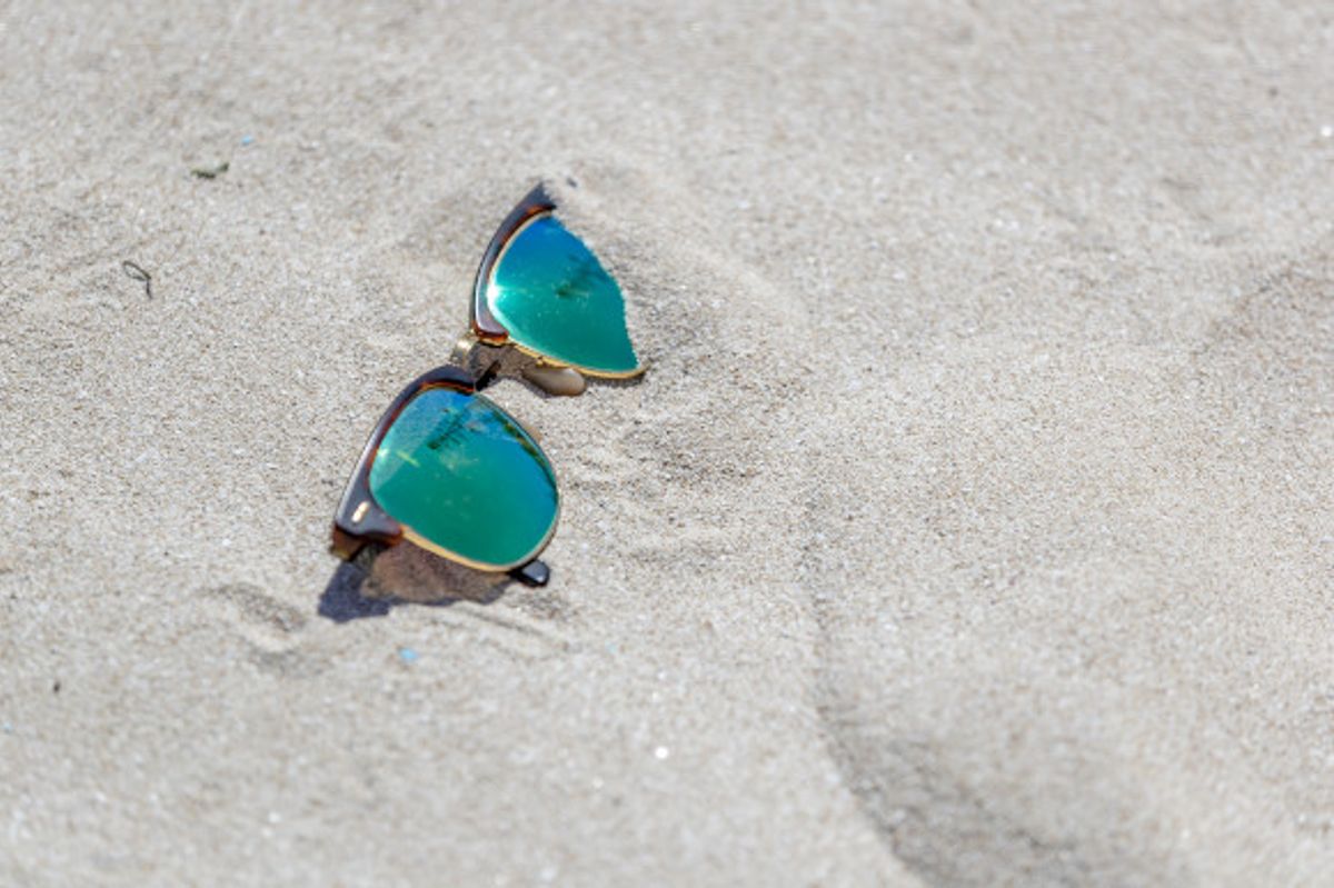 A pair of sunglasses with green lenses placed on the sand 