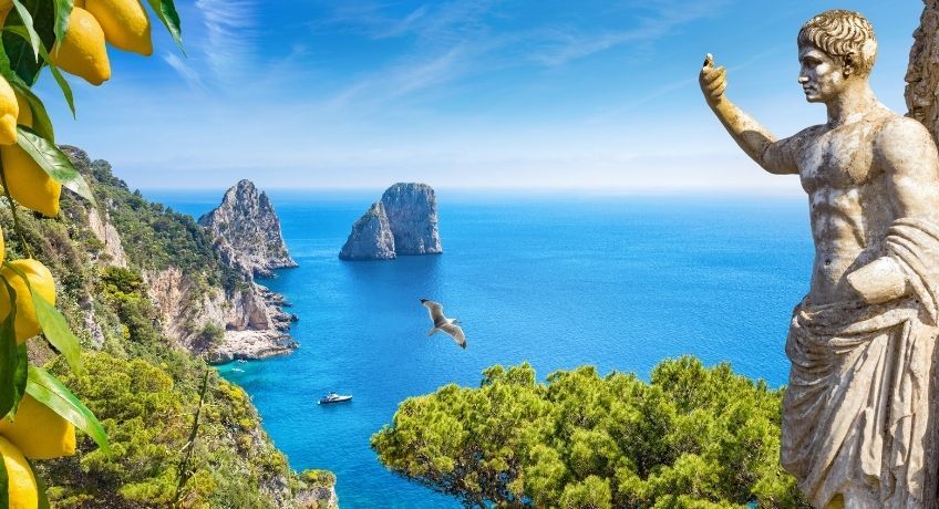 Roman looking statue overlooking rocky cliffs and clear blue waters