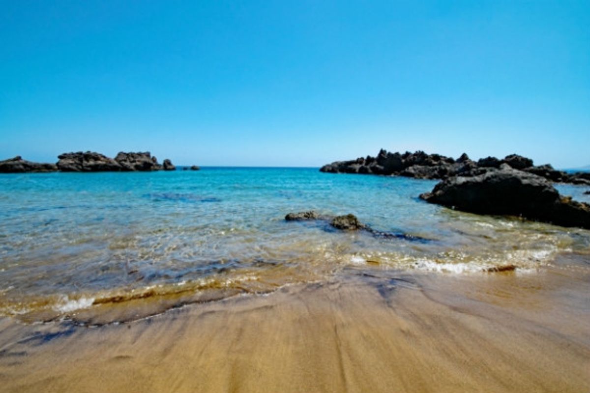Black rocks peaking out of the Mediterranean ocean on Playa Chica beach lanzarote