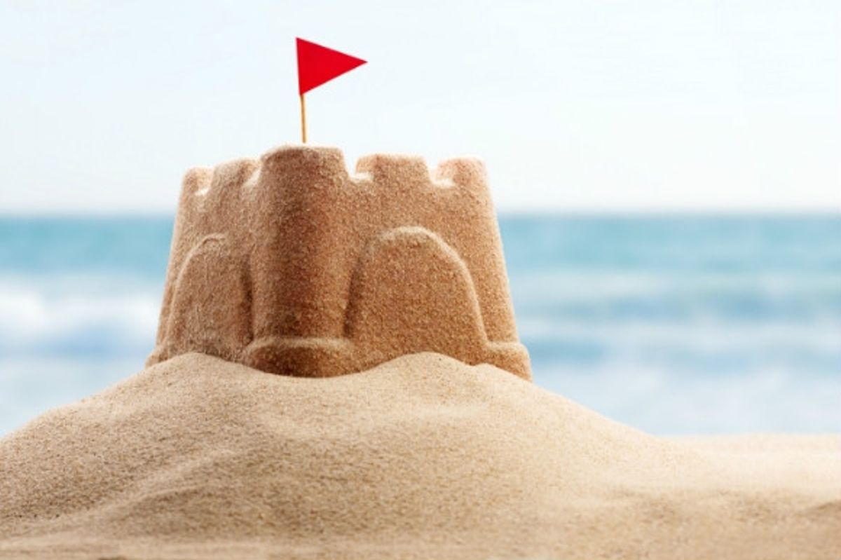 A sandcastle with a red flag perched on a spot of sand on the beach.