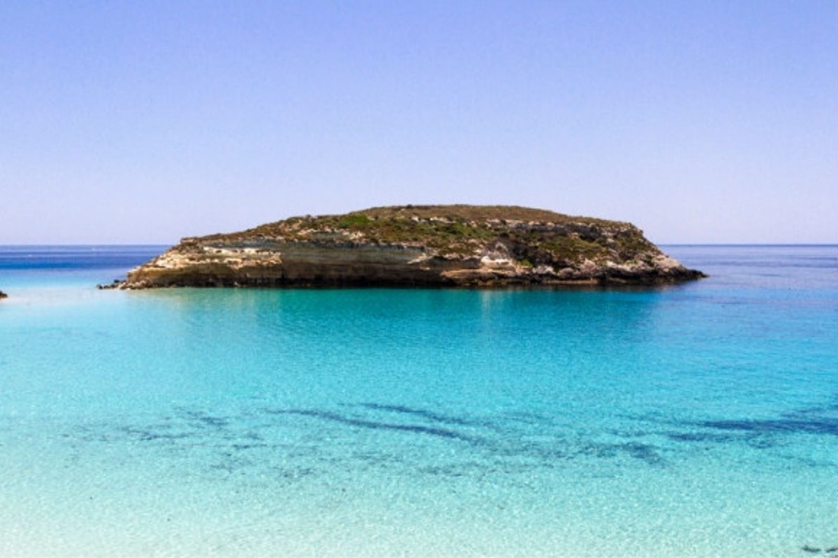 Italy's stunning clear shimmering blue waters of Rabbit Beach in Sicily with a dominating rock formation in the centre of the sea.