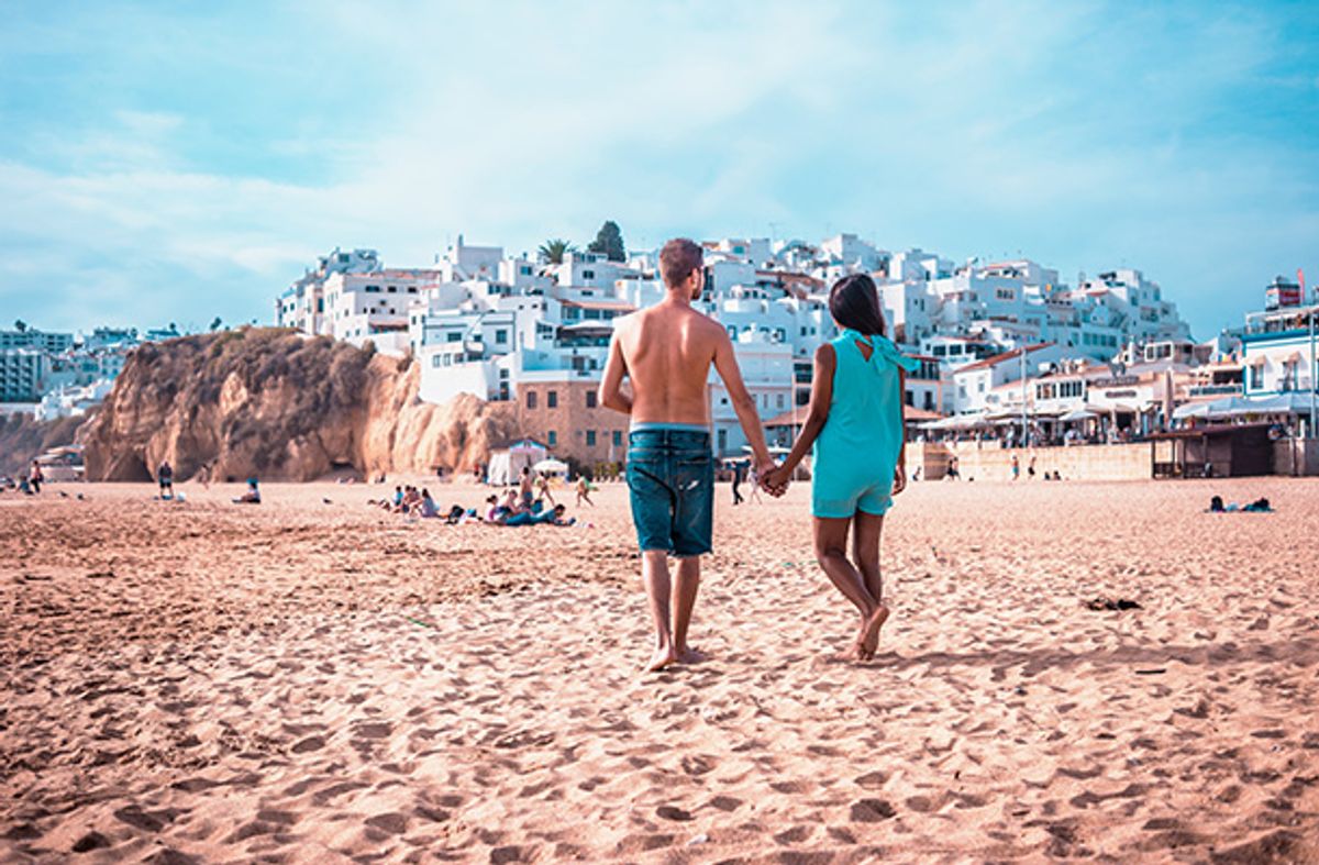 Couple walking away from the camera on a beach in Albufeira, Portugal. The whitewashed buildings of Albufeira town form the background.