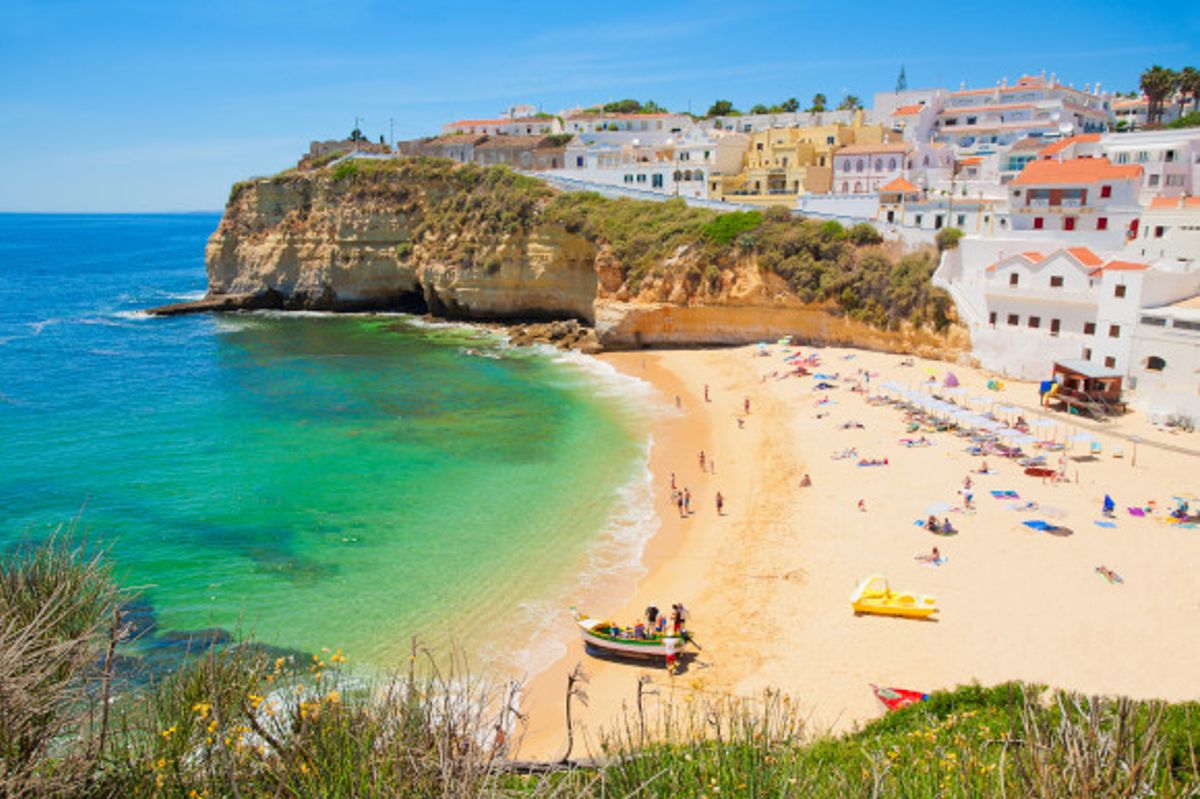 A beautiful beach in Portugal's Algarve with a wide stretch of golden sand and cliffside houses looking over the Atlantic Ocean
