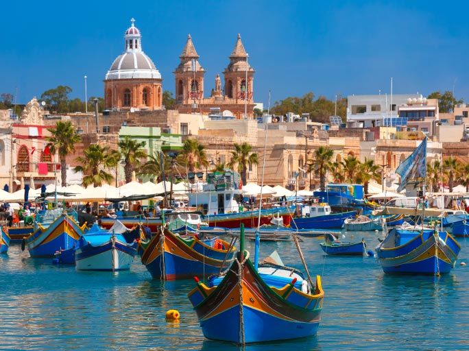 Colourful boats in the sea with traditional buildings in the background