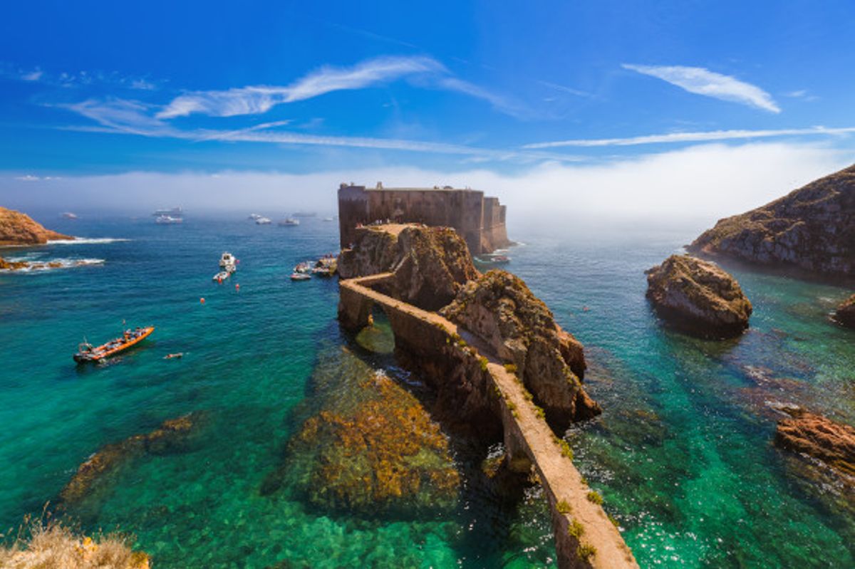 The azure waters and fort of Praia do Carreiro do Mosteiro Beach in Portugal surrounded by boats and rocks 