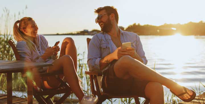 Couple with their phones sitting by a lake at sunset