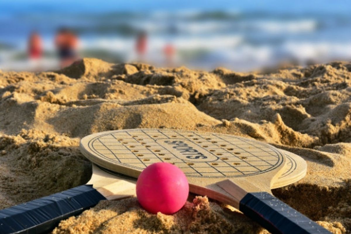 Two bats and a pink ball laid on the beach.