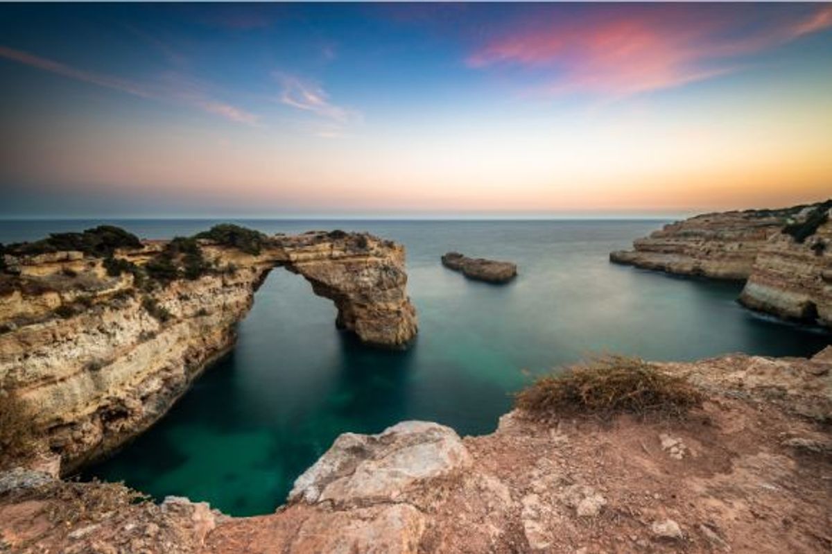 A beautiful pink and orange sunset over Praia de Albandeira Beach in Portugal's Algarve region
