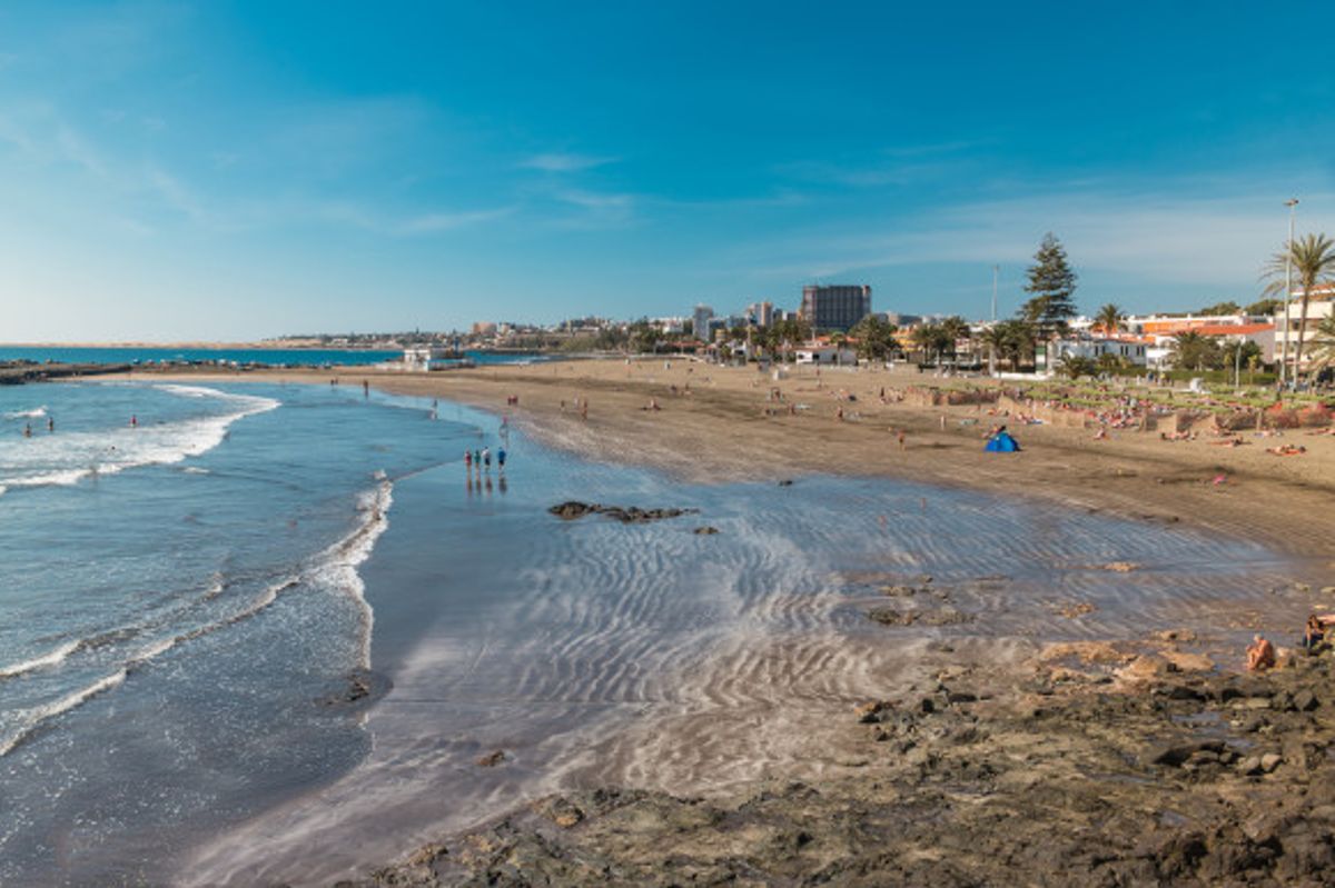 Extended view of the black tranquil sands and rippling waves at San Agustin Beach in Gran Canaria