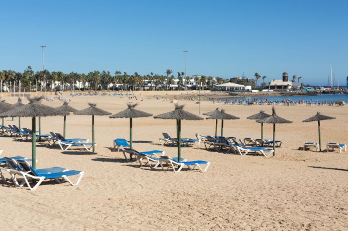Sun-soaked Caleta de Fuste beach accessorised with sunloungers and straw unbrellas on a sunny day in Fuerteventura