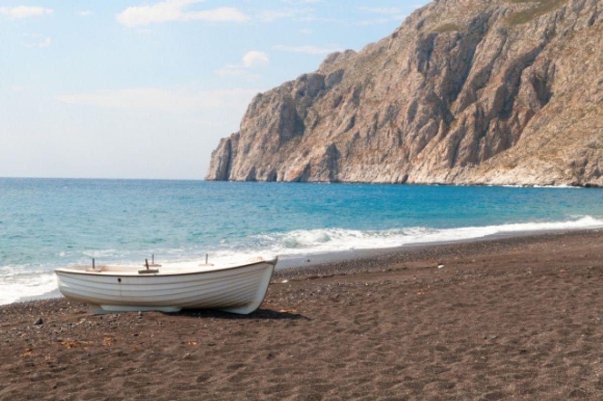 View of Kamari Beach in Santorini with a boat sitting on the sand and a tall cliff overlooking the water