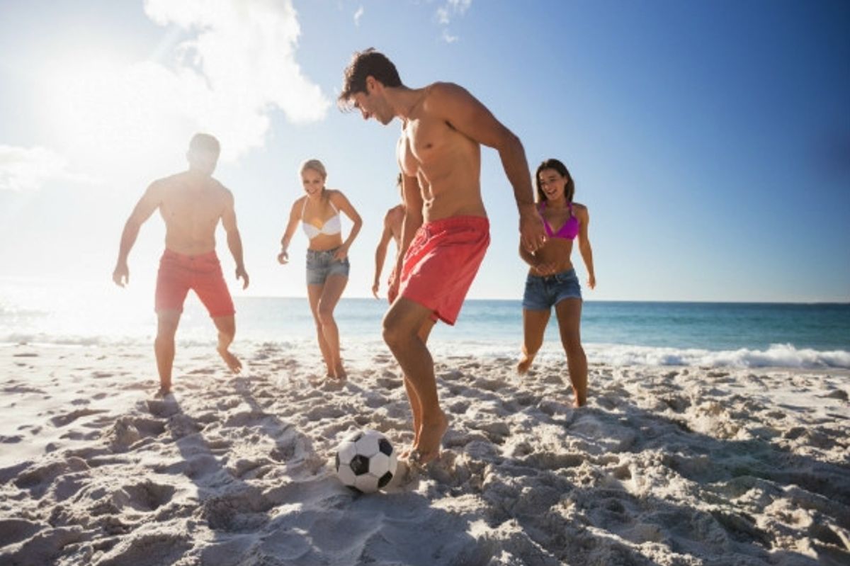 Friends playing football on the beach on a sunny day.