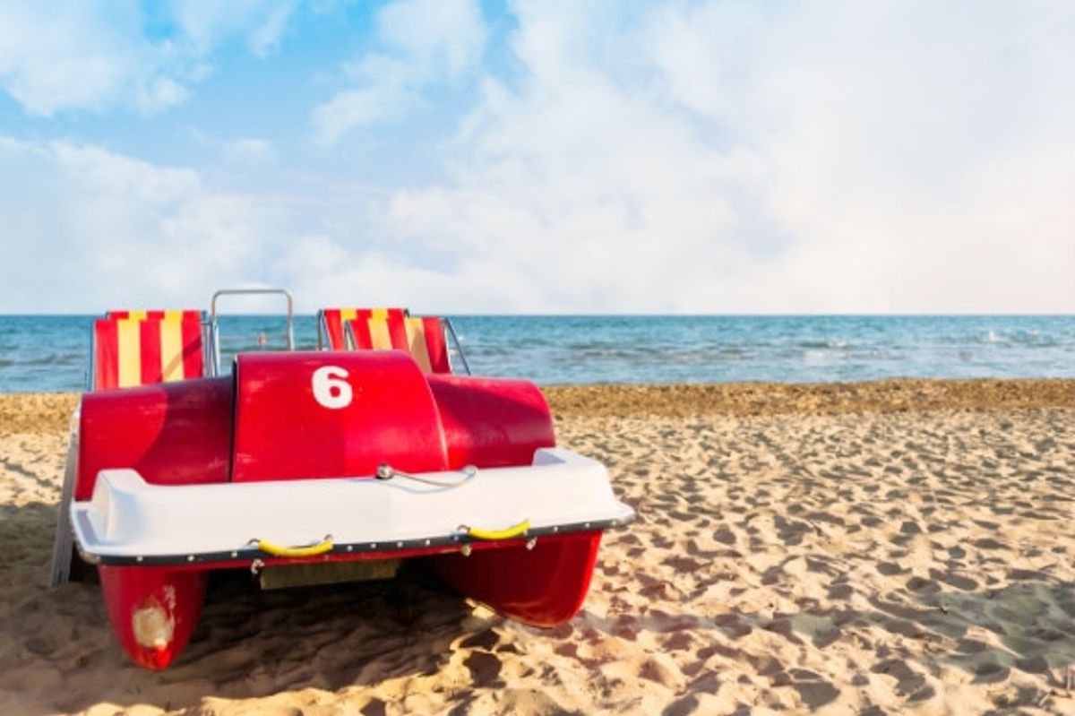 Red peddle boat on the beach with the sea in the background.