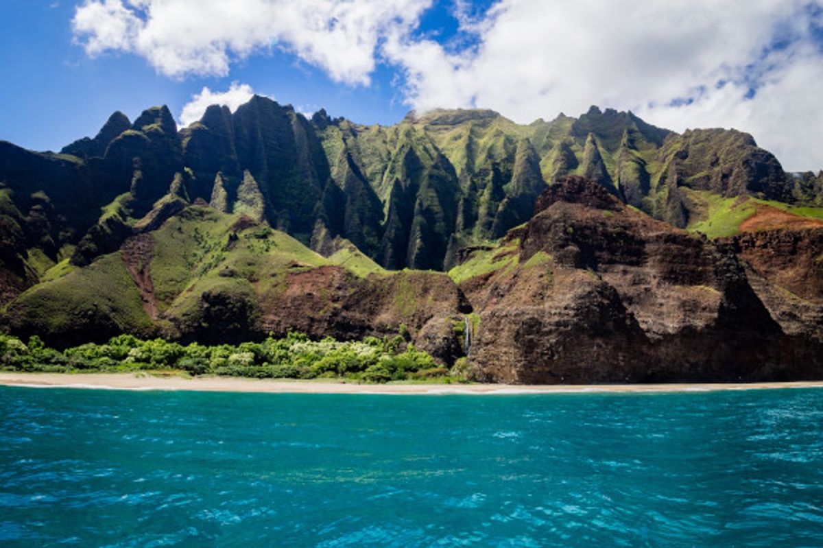 The striking Honopu Beach in Hawaii backed by dramatic volcanic cliffs with shimmering blue waters fronting the sand