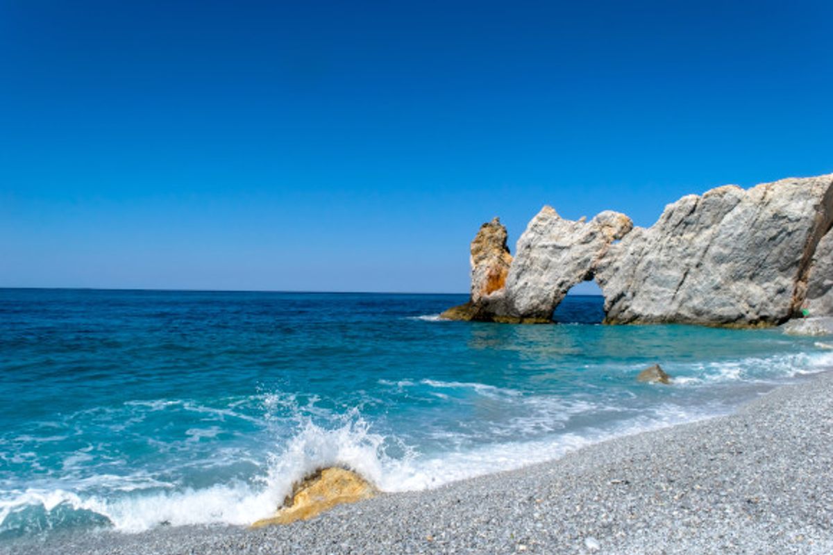 The pebbly Lalaria Beach in Skiathos with cliffs sitting in the water and waves lapping the shore