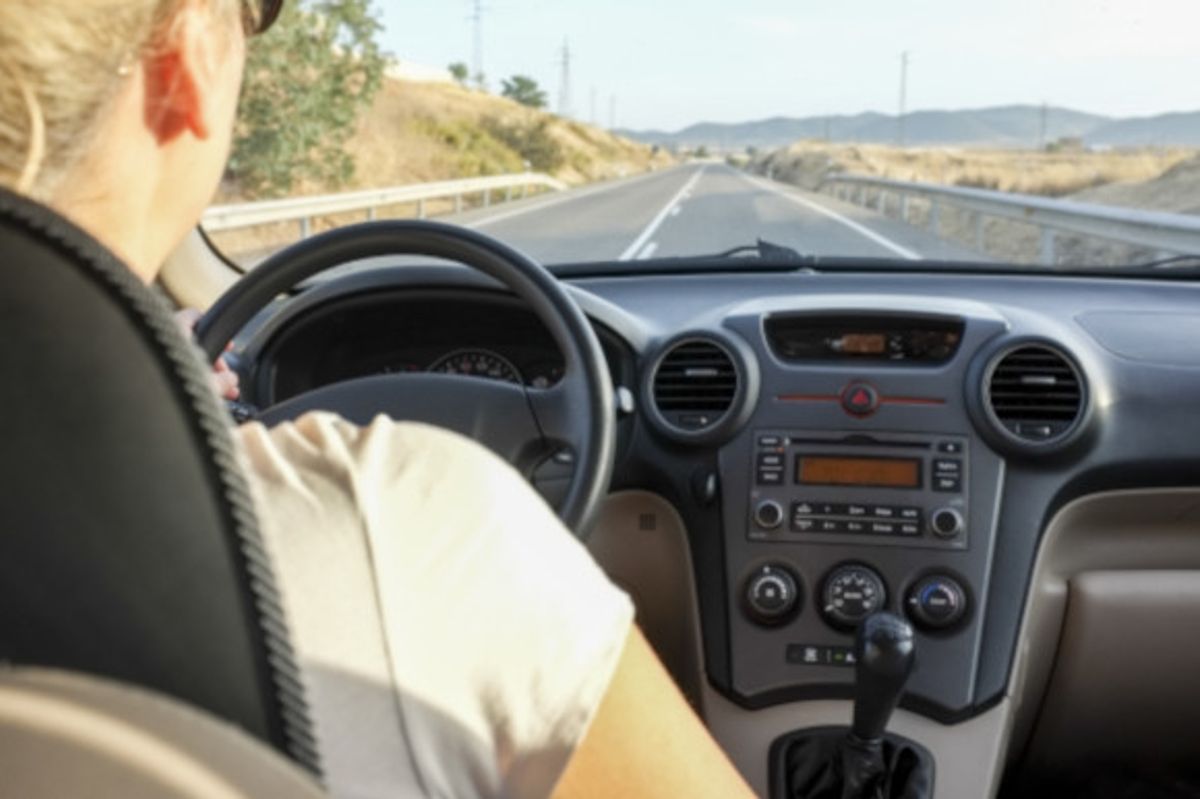 Woman driving on a clear road in Spain alongside the countryside wearing sunglasses on a sunny day.