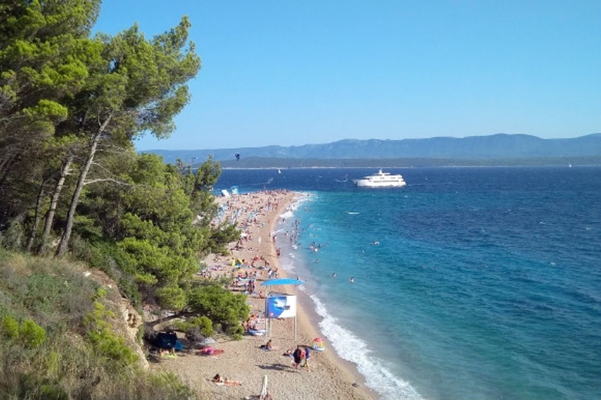 Lush green landscapes leaning over the golden stretches of Zlatni Rat Beach in Croatia.