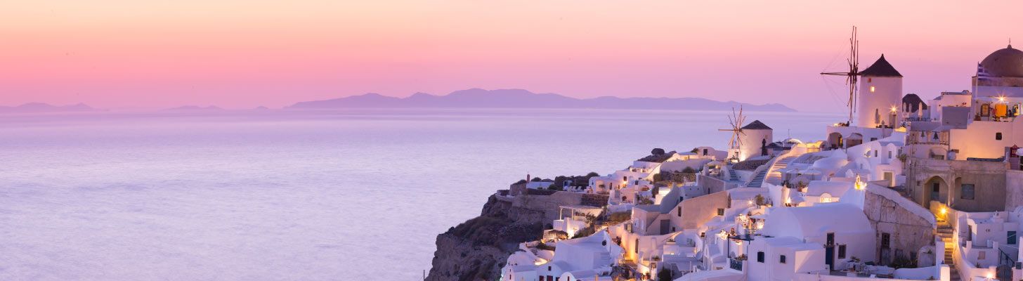 Windmills & traditional white buildings overlooking the sea at sunset in Santorini