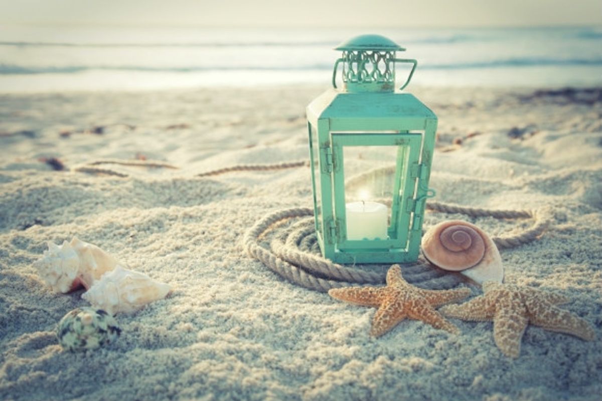 Lantern, shells and star fish nestled in the soft grains of sand on the beach.