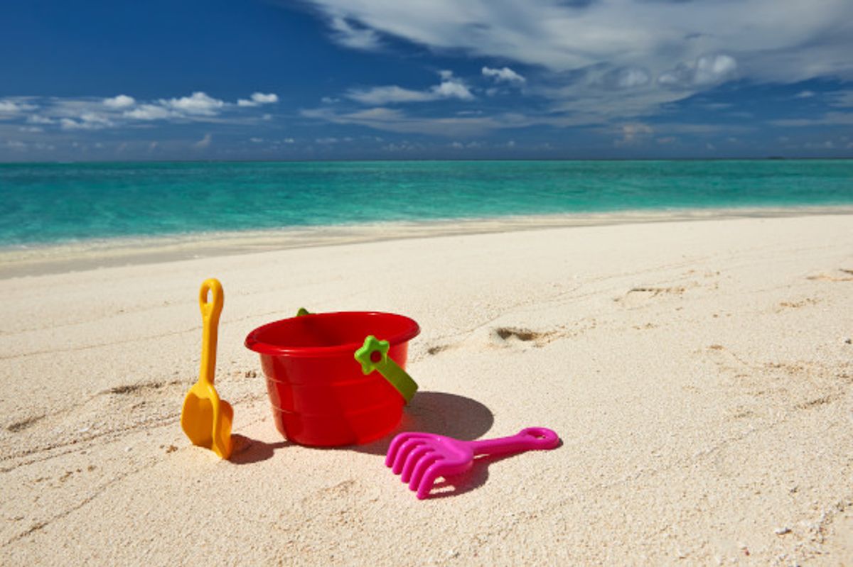 Bucket and spade set placed on a stretch of beach with the ocean and blue skies in the background