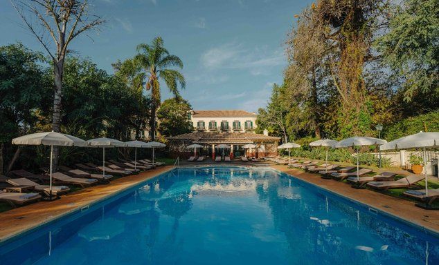 An outdoor swimming pool heading towards a historic looking Quinta with sun loungers surrounding the swimming pool