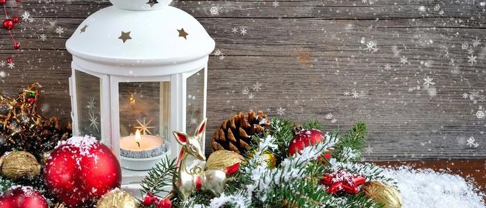 Holiday decoration scene with white lantern, pine cones, and snow.