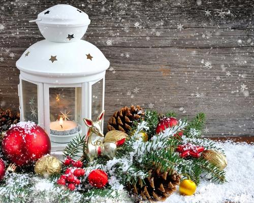 Holiday decoration scene with white lantern, pine cones, and snow.