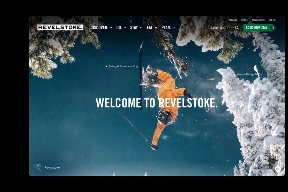 The seerevelstoke.com home page in winter: a skier mid-air above snowy trees, with pins linking to skiing and winter things to do