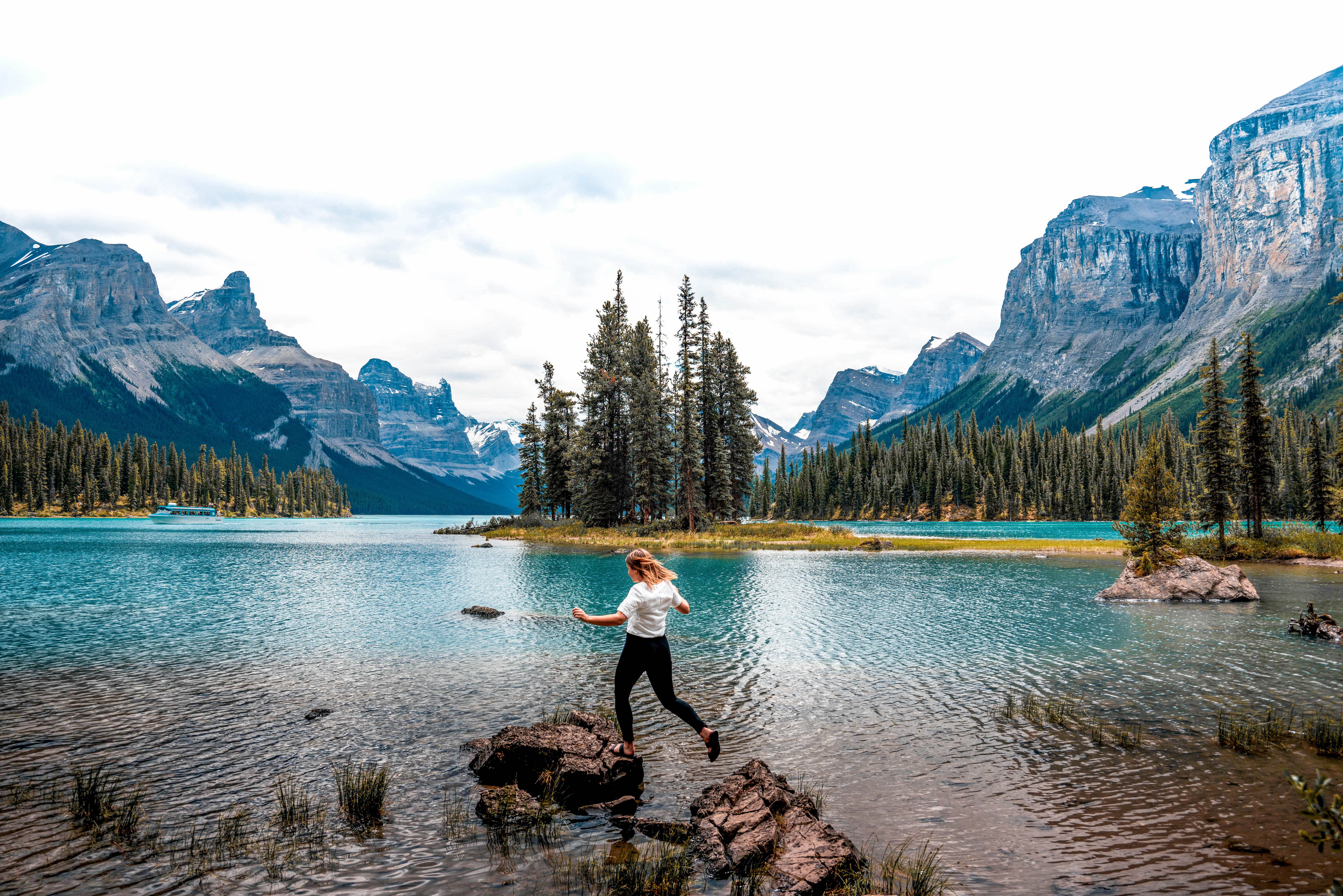 A hiker hopping across rocks in Maligne Lake, with Spirit Island behind