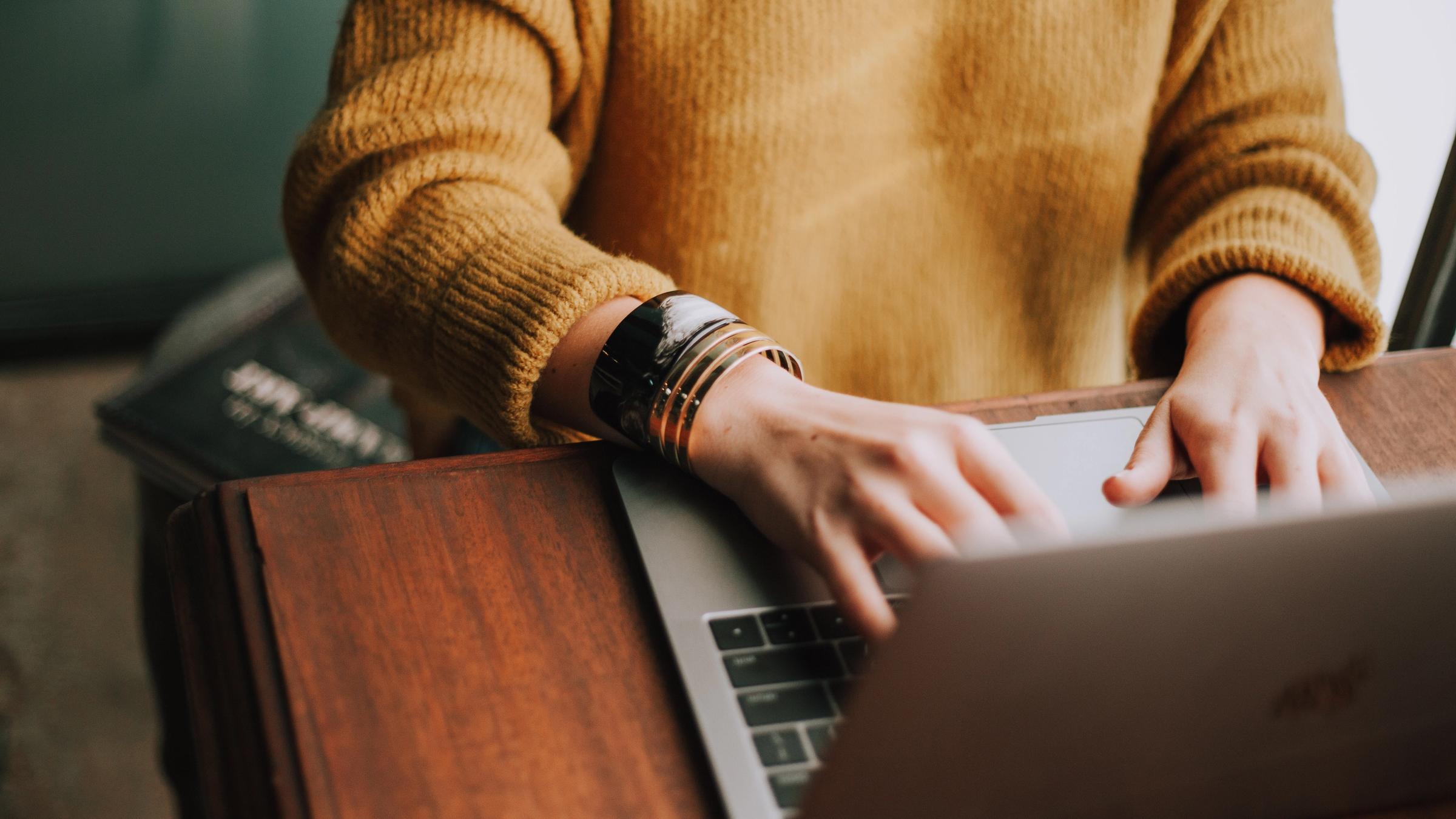 Someone in a mustard sweater typing on a laptop