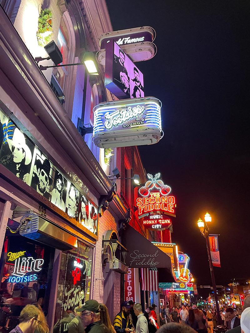 Neon signs for Tootsie’s and The Second Fiddle over a busy Broadway at night.