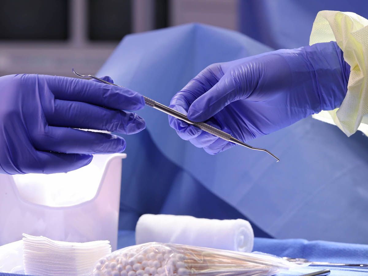 Gloved hands holding medical tweezers over sterile supplies
